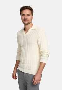 Maglione girocollo color crema, caratterizzato da una texture a coste, scollatura a V e maniche lunghe, abbinato a pantaloni grigi. Design semplice e rilassato.