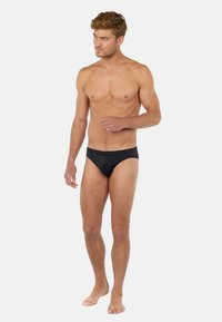 Černé plavky s nízkým pasem, hladkým povrchem a minimalistickým stylem, s elastickým pasem a bez viditelných vzorů.