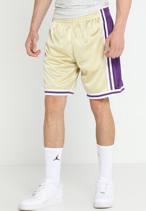 Mann, der beige Basketballshorts mit lila und weißen Streifen, weiße Crew-Socken mit schwarzem Logo und weiße Sportschuhe trägt.