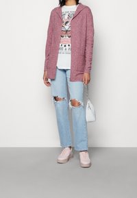 Lange mouwen, hoodie cardigan in gemaroonde brei; gecombineerd met een graphic tee, vergrijsde lichtblauwe jeans, pastelroze sneakers en een kleine witte tas.