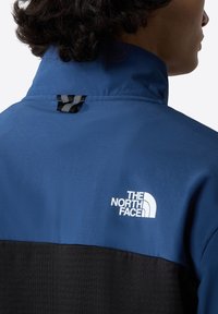 Blue and black jacket featuring a high collar, smooth fabric, and The North Face logo in white on the upper back. полосны.
