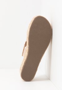 Sandale beige avec des détails en jute tressé et une semelle en caoutchouc texturé, présentant un design plat et une bride sécurisée à la cheville.