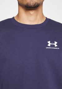 T-shirt in cotone blu navy con collo a giro, con un logo bianco di Under Armour sul petto. Tessuto liscio con maniche corte.