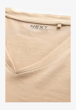 T-shirt beige à manches courtes avec un col en V, fabriqué en tissu coton lisse. Présente une étiquette imprimée avec le nom de la marque "NEXT."