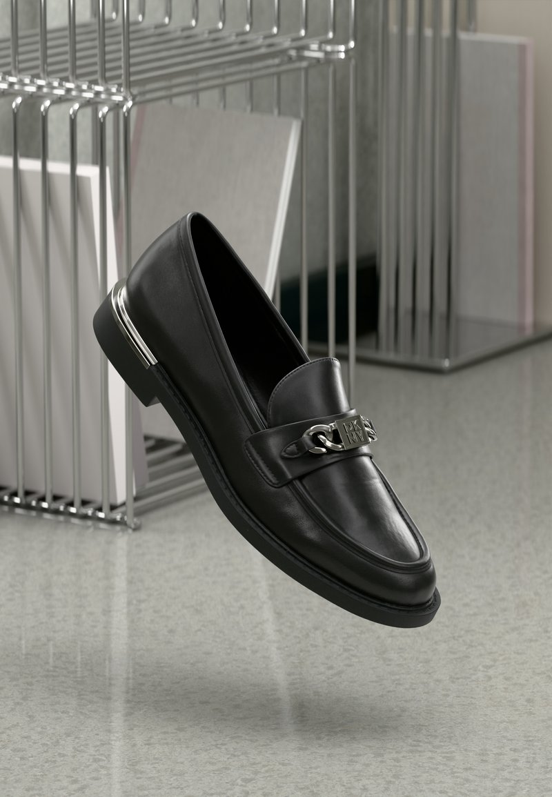 Musthave nahkased mustad loafersid, millel on ümar nina, lame tald ja metallne aksent rihmal. Kingal on sile tekstuur ja poleeritud viimistlus.