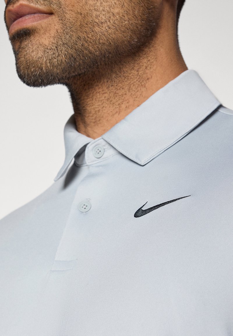Hellblaues Nike Polohemd mit einem kragenförmigen Design, zwei Knöpfen und einem schwarzen Swoosh-Logo auf der linken Brust. Glattes, strukturiertes Gewebe.