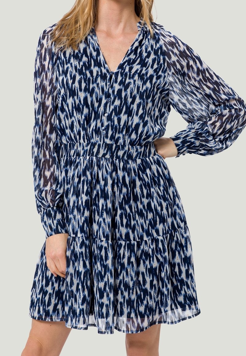 Robe à manches longues avec un motif abstrait bleu marine et blanc. Fabriquée en tissu léger, elle dispose d'un col en V avec boutons et d'une jupe à volants.