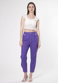 Witte eyelet crop top met ruches mouwen, gecombineerd met paars hoge taillebroek met zijzakken en gouden knoopaccenten.