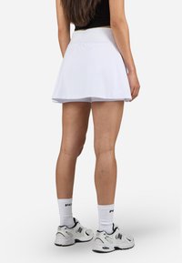 Valge skort, millel on voolav disain ja elastne vöökoht, koos valgete spordisokkide ning mustade aktsentidega kingadega.