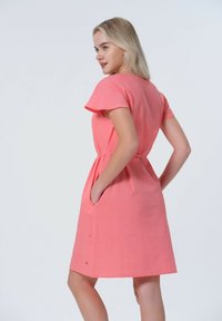 Koralli mekko lyhyillä hihoilla, kapealla vyötäröllä, taskuilla ja polvipituisella helmaa. Suloinen tekstuuri, jossa on minimaalinen yksityiskohtaisuus.