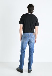 Black polo shirt with white trim, paired with light blue denim jeans. Black shoes, visible stitching and back pocket details on jeans.