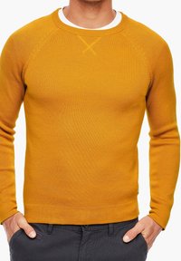 Senfgelber, gestrickter Pullover mit Rundhalsausschnitt, gerippter Struktur und Raglanärmeln. Mit einem dezenten Kreuzstichdetail am Hals.