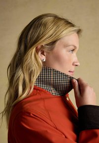 Czerwona kurtka z w kratkę wewnętrznego kołnierza. Kołnierz ma czarno-biały wzór, a kurtka posiada ribbowe czarne mankiety. Szczegół z metalowymi guzikami.