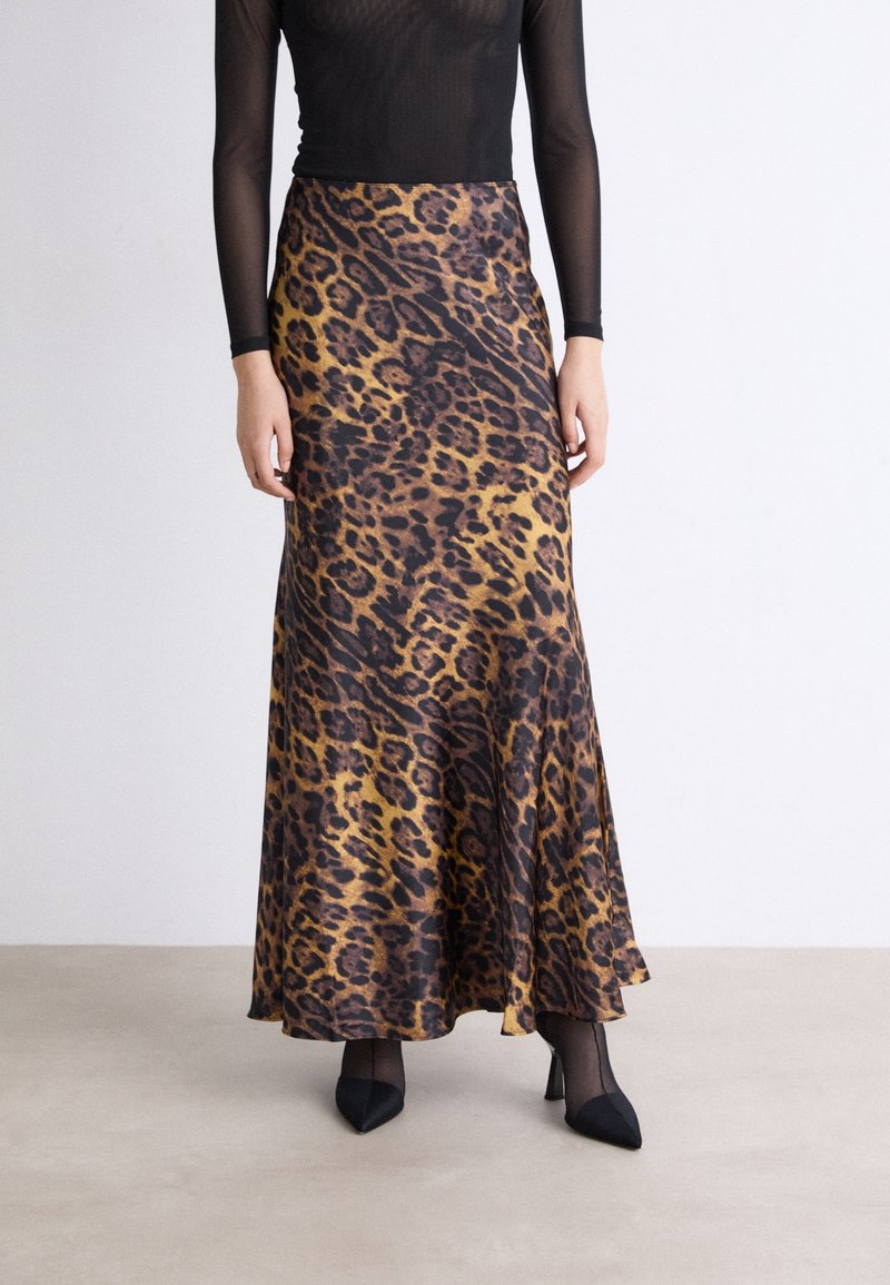 Falda maxi de estampado de leopardo en marrón y negro, material sedoso, diseño acampanado, cintura de altura media, combinada con tacones negros de punta y blusa transparente.