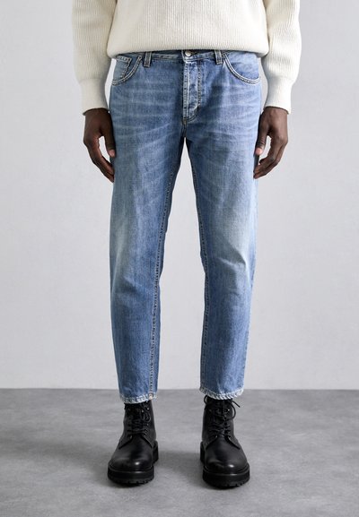 Jeans in denim blu chiaro con taglio dritto, finitura sbiadita e leggere pieghe, abbinati a stivali da combattimento neri con lacci.