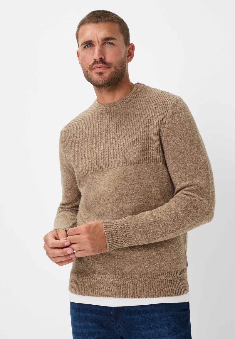 Sweter dzianinowy w jasnobrązowym kolorze z żebrową teksturą na ramionach i mankietach. Dopasowany fason z okrągłym dekoltem, noszony na białej koszuli.