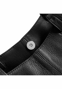 Interno di una borsa in pelle nera con cuciture visibili, dotata di una chiusura a scatto rotonda in metallo argento. La superficie testurizzata aggiunge profondità.
