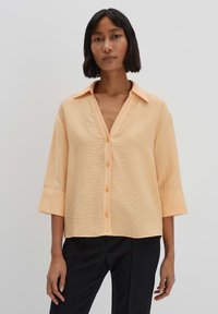 Blusa di colore pesca, con texture, colletto a punta, maniche a tre quarti e chiusura a bottoni. Tessuto morbido e vestibilità comoda.