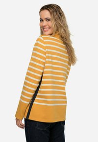 Maglietta a maniche lunghe a righe gialle e bianche con colletto a lupetto, spacchi laterali e vestibilità casual, abbinata a jeans di denim scuro.