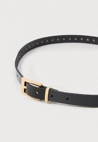 Musta nahkavyö sileällä pinnalla, jossa on kultainen metallipanta ja useita säätöreikiä hihnassa.