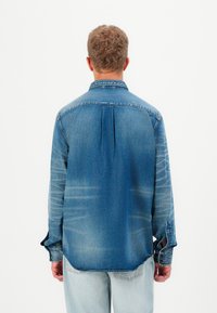 Helesinine denimpusa pika varrukaga ja nööpidega kraega. Omab selja voldikut ja kerget tuhmumist tekstuuri jaoks.