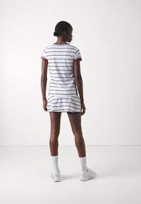 Vestido blanco a rayas con acentos en rojo y azul marino, que presenta mangas cortas, un dobladillo con volantes en capas y un diseño ajustado, combinado con zapatillas blancas.