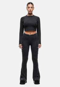 Zwarte crop top en bijpassende flared broek van textuurstof. De outfit heeft stikdetails en een aansluitende pasvorm.