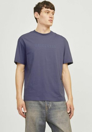 Marineblå bomulds T-shirt med korte ærmer, der har prægede "ORIGINALS" tekst på tværs af brystet, kombineret med lysvaskede jeans.