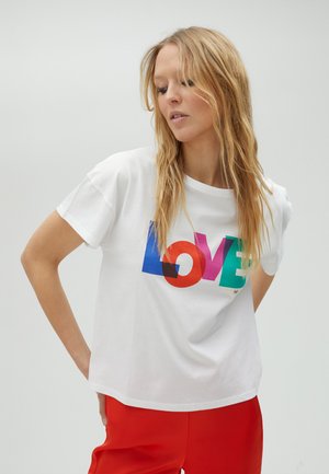 Camiseta blanca de algodón con un gráfico colorido de "AMOR" en azul, rojo, púrpura y verde. Diseño de mangas cortas y ajuste holgado.