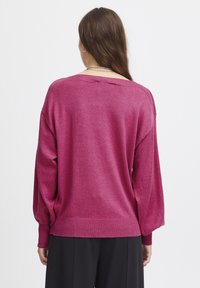 Överdimensionerad tröja i magenta med ribbade ärmslut och nederkant. Mjuk textur, sänkt axel och vid halsringning. Bakifrån visad.