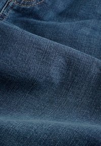 Mörkblå denimtyg med en lätt strukturerad yta och subtila blekningsmönster, som visar naturliga sömmar och veck.
