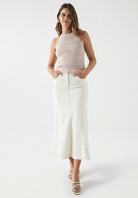 Top de tirantes ajustado en rosa claro combinado con una falda midi de mezclilla blanca que tiene bolsillos y detalles de costura visibles; el modelo lleva sandalias blancas de tiras.