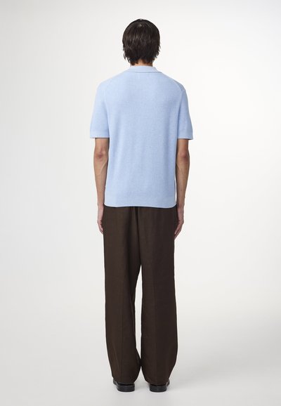 Vaaleansininen lyhythihainen neulepaita, jossa on ribbitekstuuri. Yhdistetty väljiin ruskeisiin housuihin. Yksinkertainen muotoilu, ei näkyviä kuvioita.