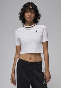 White cropped t-shirt made of cotton with short sleeves, featuring a black Jordan logo on the left chest. Black joggers with white side stripes.