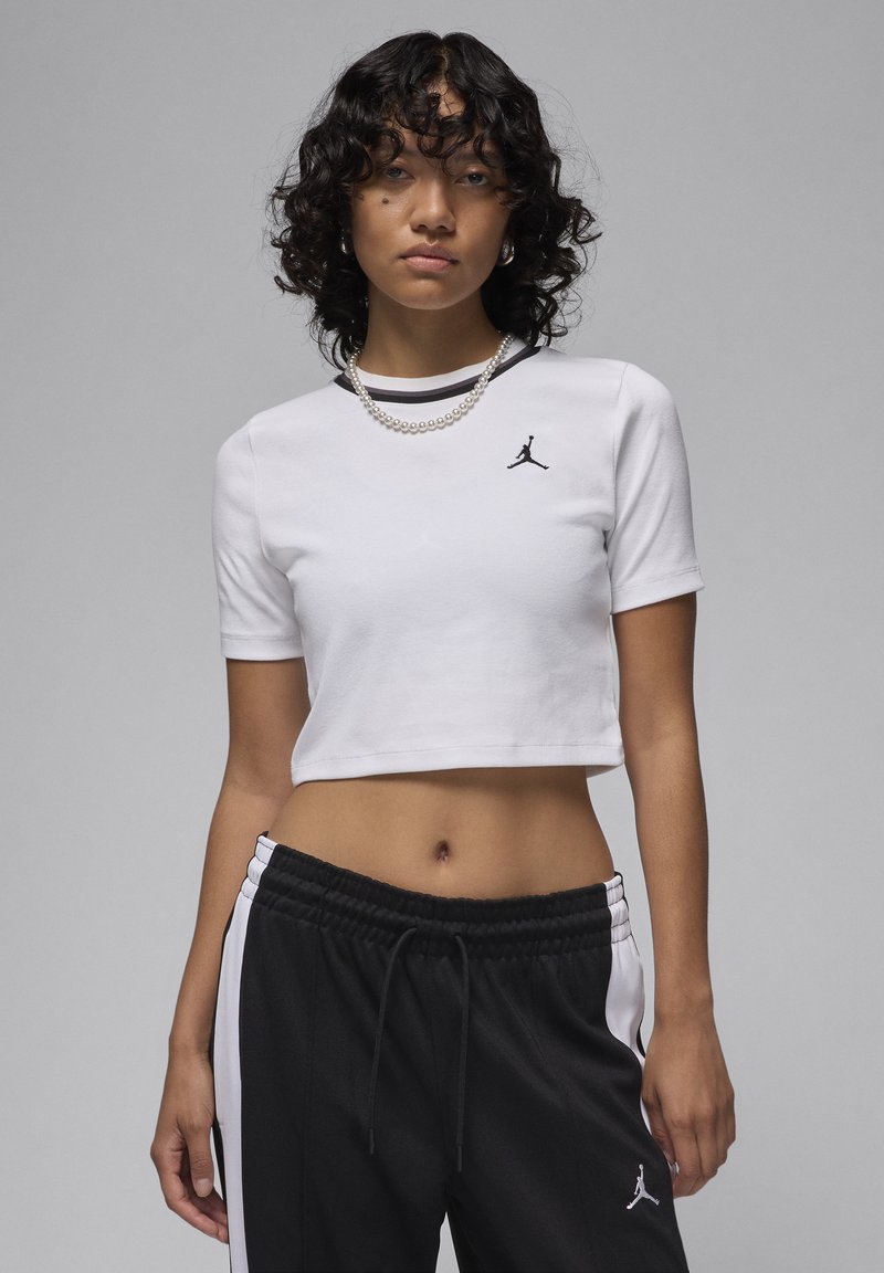 White cropped t-shirt made of cotton with short sleeves, featuring a black Jordan logo on the left chest. Black joggers with white side stripes.