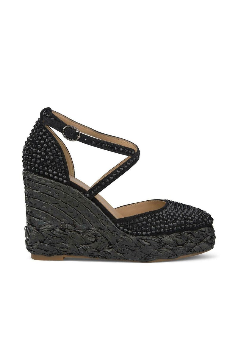 Sandalia de cuña espadrille negra con plataforma tejida texturizada y parte superior con tachuelas. Presenta correas de tobillo entrelazadas y punta redondeada.