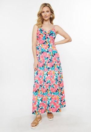 Maxi dress featuring a vibrant floral pattern in pink, blue, and orange, with thin straps, a fitted bodice, and a tiered bottom. Worn with tan sandals.
