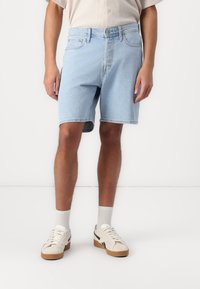 Light blue denim shorts with a classic cut, five-pocket design, and a raw hem. Worn with white sneakers and light gray crew socks.