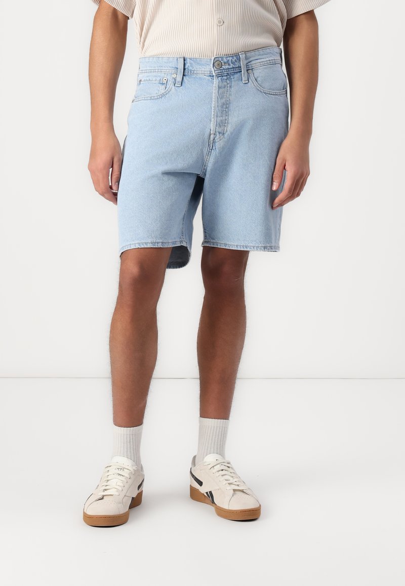 Light blue denim shorts with a classic cut, five-pocket design, and a raw hem. Worn with white sneakers and light gray crew socks.