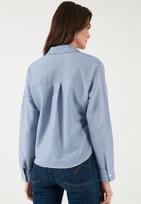 Striped button-up shirt in light blue and white. Features a back pleat, long sleeves with cuffs, tailored fit, and smooth cotton material.