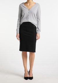 Grauer gestrickter Cardigan mit V-Ausschnitt und Knöpfen, kombiniert mit einem schwarzen Bleistiftrock. Schwarze High-Heels runden das Outfit ab.