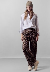 Camisa blanca de botones, pantalones de leopardo marrón, zapatillas beige y un gorro de punto beige. Corte relajado con texturas de tela visibles.