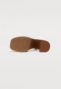 Brune hæl sandal med en tekstureret gummisål, der har en glat overdel og en ankelrem. Sålen viser et mønstret dæk for greb.