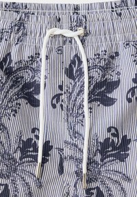 Gros plan sur un short en tissu rayé avec un motif floral bleu marine et un cordon blanc noué à travers des œillets métalliques.