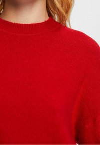Roter Strickpullover mit rundem Halsausschnitt und gerippten Bündchen. Weiche Textur, mittleres Gewicht und glatte Oberfläche ohne sichtbare Muster.