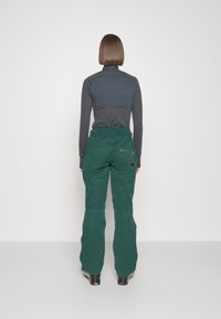 Groene waterdichte broek met een ontspannen pasvorm, voorzien van meerdere zakken en een gladde textuur, gecombineerd met een donkergrijze lange mouwtop.