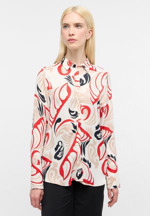 Blusa a maniche lunghe con base crema e motivi a spirale rossi, neri e beige, chiusura con bottoni sul davanti e colletto classico.