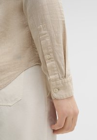 Licht beige overhemd met lange mouwen van een gemêleerde stof, met knopenmanchetten en een ronde zoom, gecombineerd met lichte broek.
