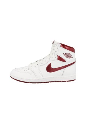 Biele kožené tenisky s vysokým strihom, s červeným Nike swoosh, akcentmi a perforovaným prstovým boxom. Obsahuje biele šnúrky a gumovú podrážku.