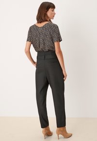 Pantaloni neri a vita alta con una texture liscia, abbinati a una maglietta a maniche corte con un motivo scuro e scollatura a barca.